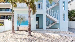 A modern building with a staircase, palm trees, and a beach view. - 4BR Beachfront Balcony Condo | Partial Ocean View (Indian Shores)