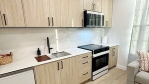 A modern kitchen with light wood cabinets, a black microwave, a sink, and a built-in oven. - The Nest @ Dovetail Cozy Condo in the Hill Country (New Braunfels)