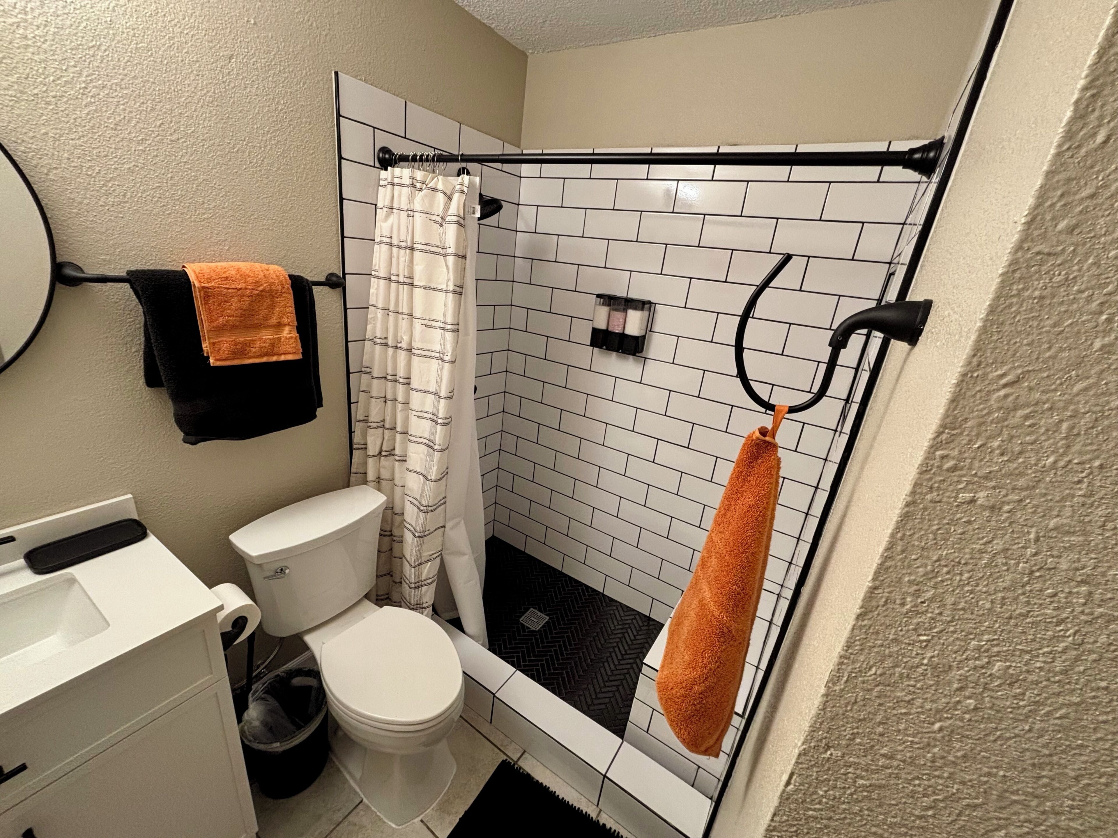 Une salle de bain avec des toilettes blanches, une douche avec un mur recouvert de carreaux noirs et blancs, et un porte-serviettes avec une serviette.
