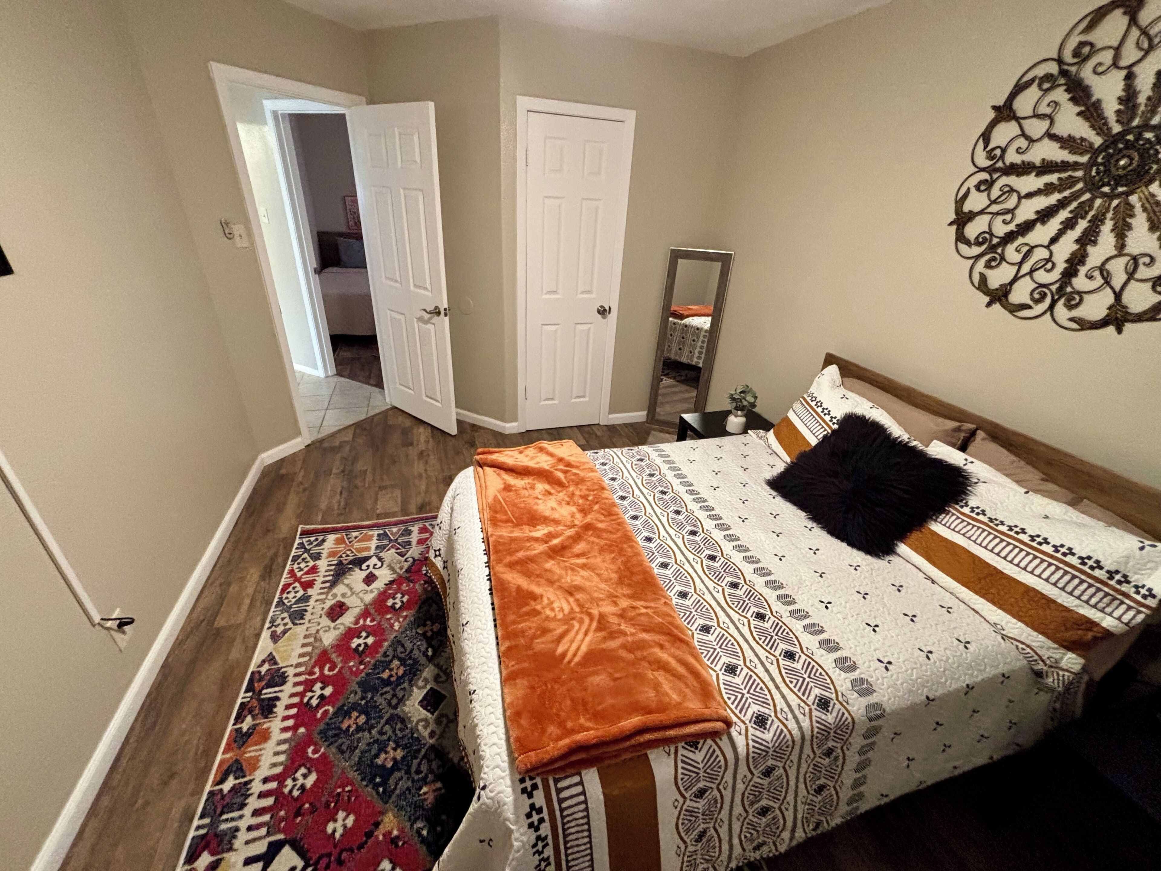 A bedroom with a bed, a rug, a mirror, and a door leading to another room.