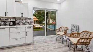 A modern kitchen with white cabinets, a coffee machine, and a view of a pool and lounge chairs through a glass door.