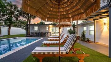 A poolside area with lounge chairs, a thatched umbrella, and a house with a visible patio.