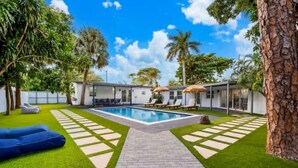 A backyard with a swimming pool, lounge chairs, and a paved walkway.