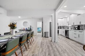 A modern kitchen with white cabinets, a dining area with a long table, and a view of the sea through an open door. - Resort Villa Modern Pool Outdoor Dining (Pompano Beach)