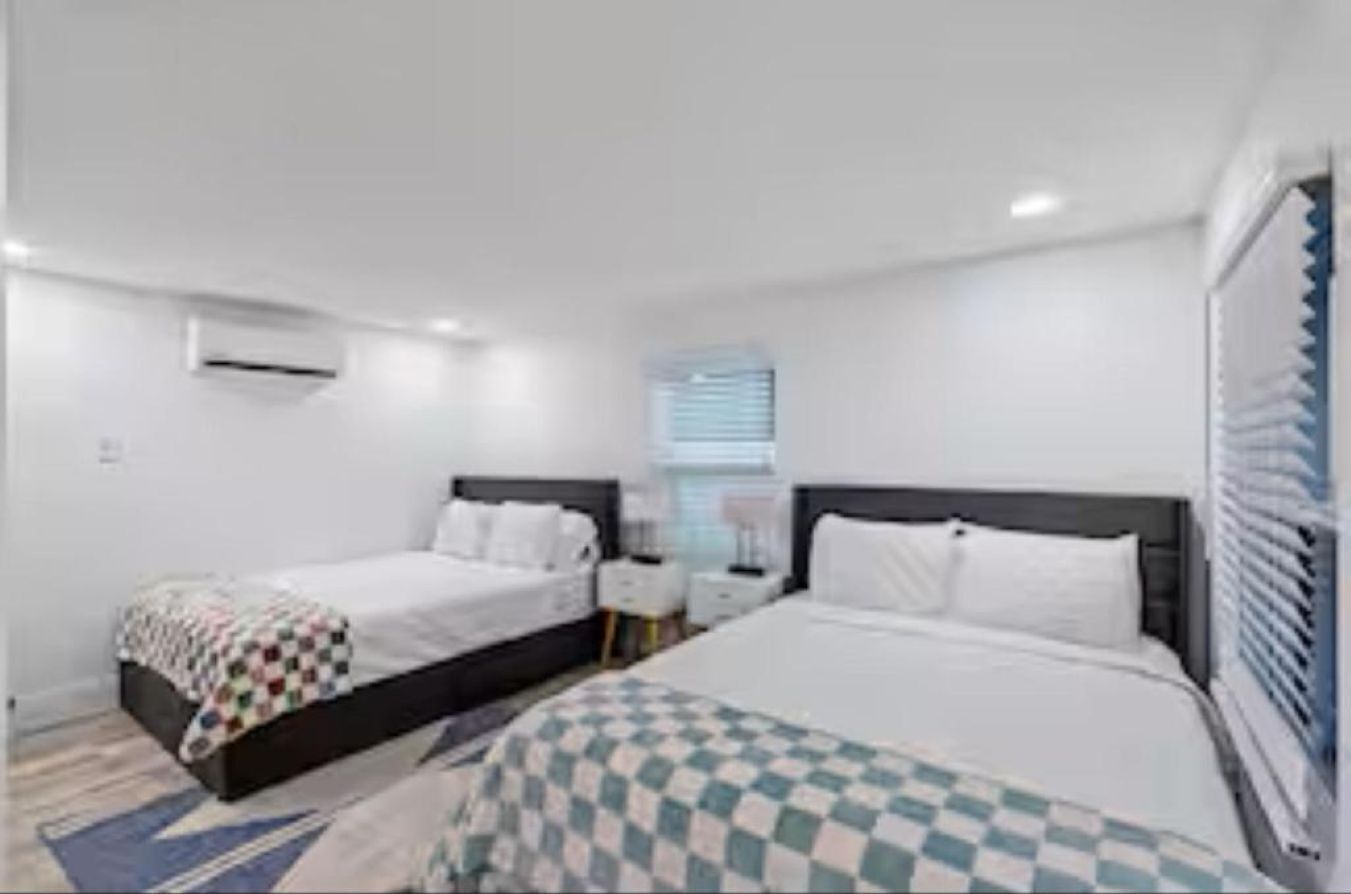 Une chambre d’hôtel avec deux lits, une fenêtre avec des stores, une table de chevet et un climatiseur fixé au mur.
