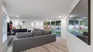 A modern living room with a sectional sofa, a flat-screen TV, and a large window offering a view of the outdoors.