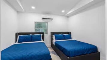 A room with two beds, white walls, and a window with blinds.