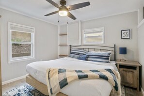 A bedroom with a bed, a ceiling fan, a bedside table with a lamp, and a window with blinds. - Beautiful Lake Front Home With Private Dock In Lick Branch Cove (Rocky Mount)
