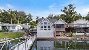 A waterfront property with a house featuring a balcony, a dock, and a small boat. - Beautiful Lake Front Home With Private Dock In Lick Branch Cove (Rocky Mount)