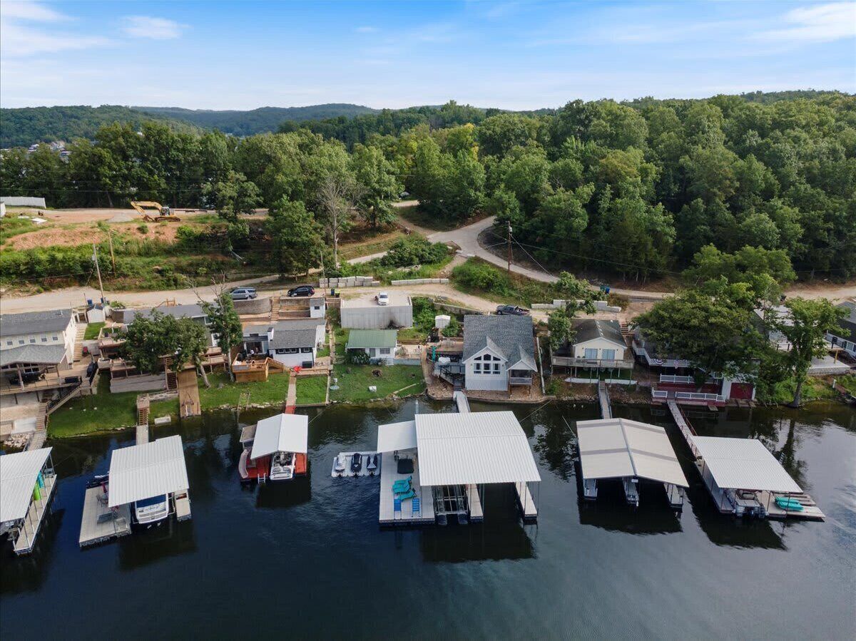 An aerial view of a lakeside community with docked boats, houses, and a forested backdrop.