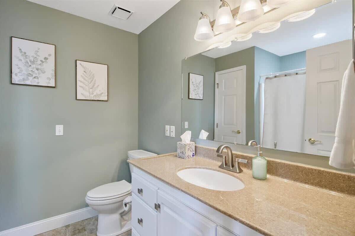 A bathroom with a white toilet, a beige countertop sink, and a large mirror.