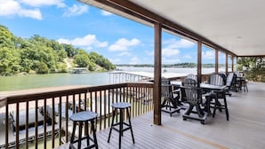 A covered deck with outdoor seating and a view of a lake and forest. - Sleeps 26 Lakefront w/ Private Dock & Dance Floor! (Lake Ozark)
