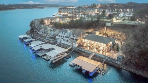 An aerial view of a waterfront property with multiple buildings, docks, and a large house with a prominent balcony. - Sleeps 26 Lakefront w/ Private Dock & Dance Floor! (Lake Ozark)