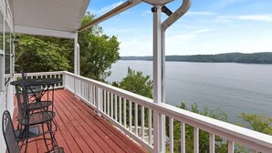A covered deck with a view of a lake, white railings, and a table with chairs. - Lakeview Manor With Historic Charm and Serene Waters (Osage Beach)