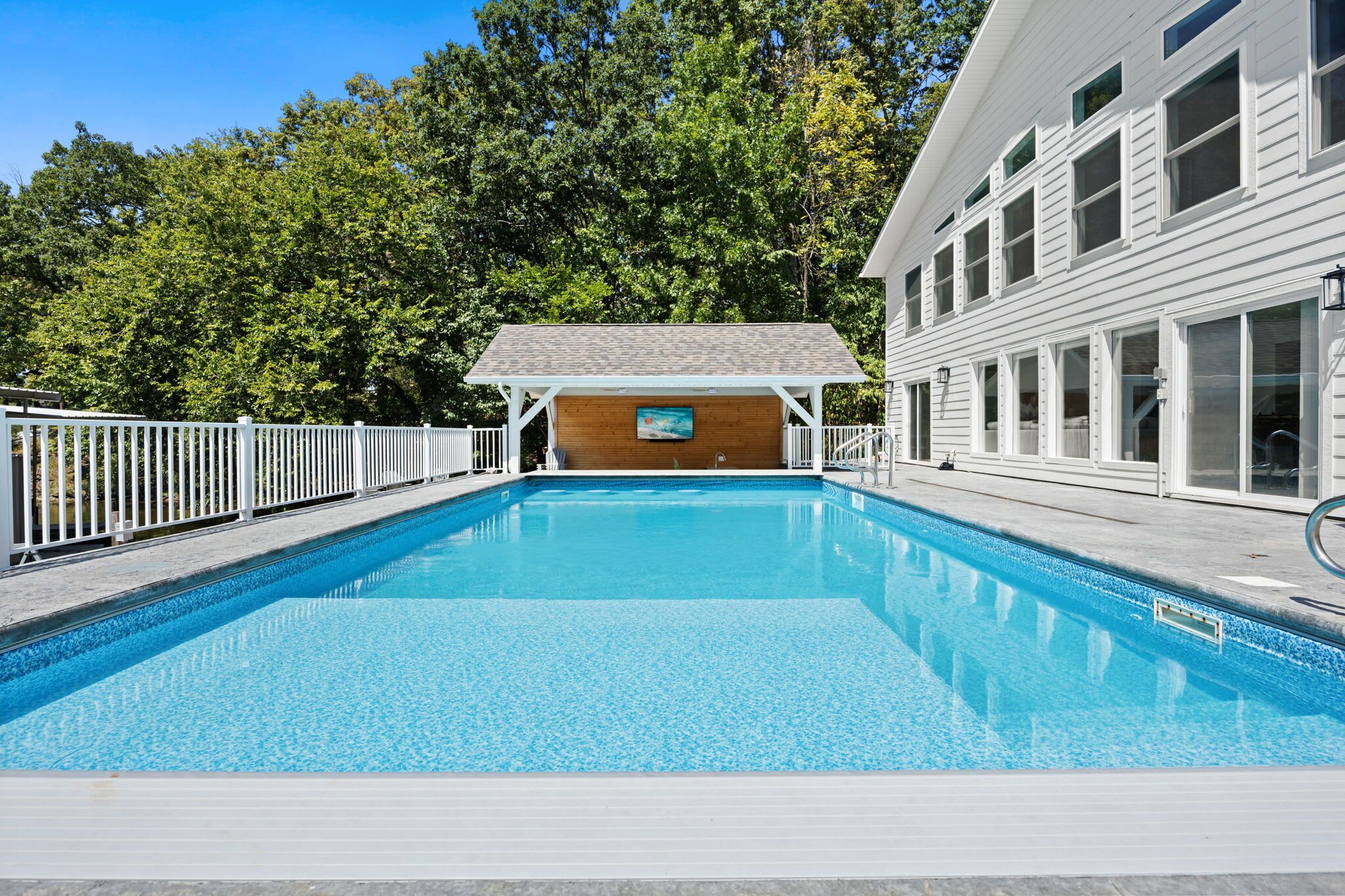 Ein rechteckiger Pool mit Holzterrasse und überdachtem Sitzbereich.