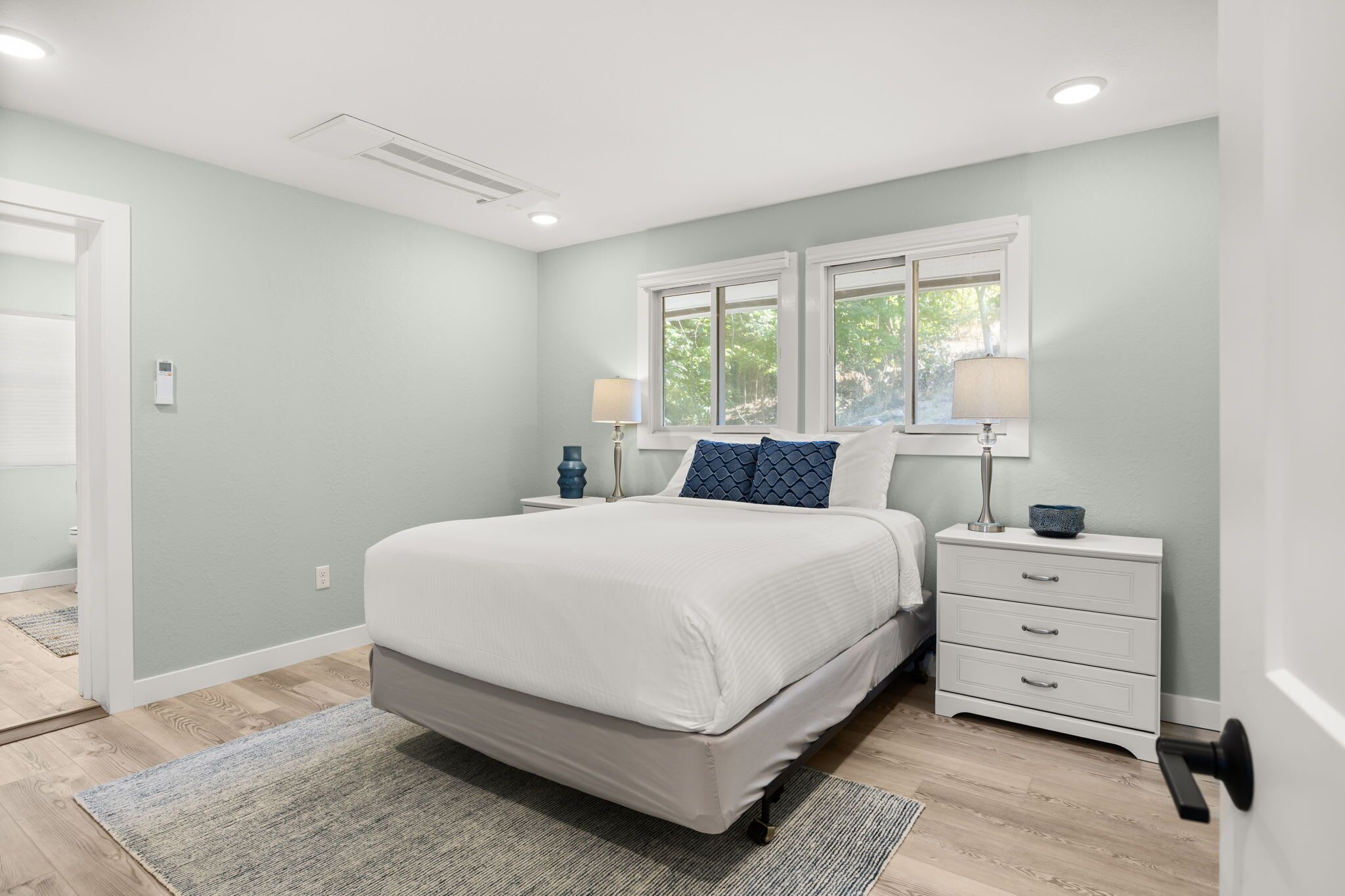 A bedroom with a bed, bedside tables, a nightstand, a lamp, and a window.