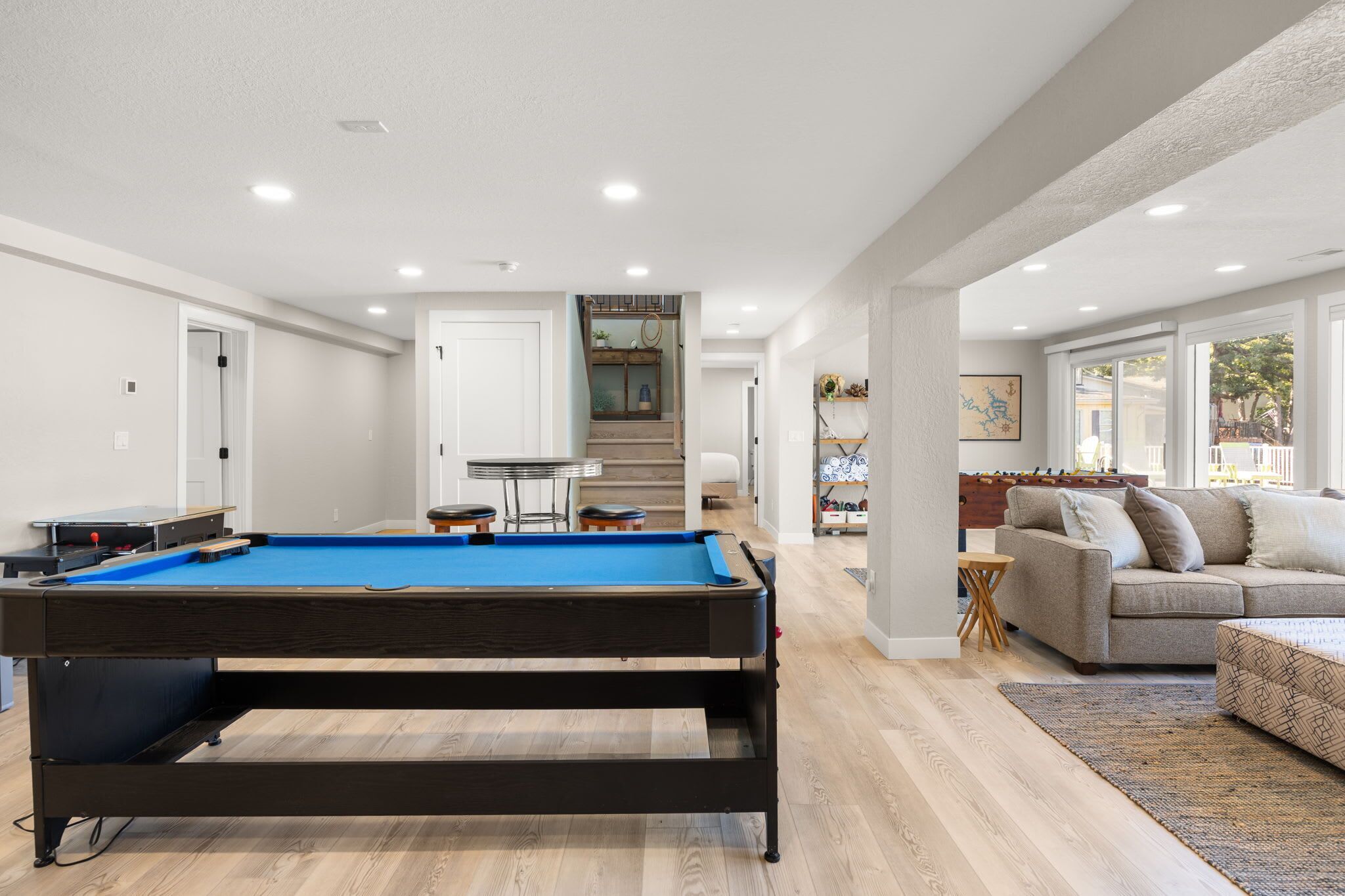 Een moderne woonkamer met een pooltafel, een bank en een trap naar een hoger gelegen verdieping.