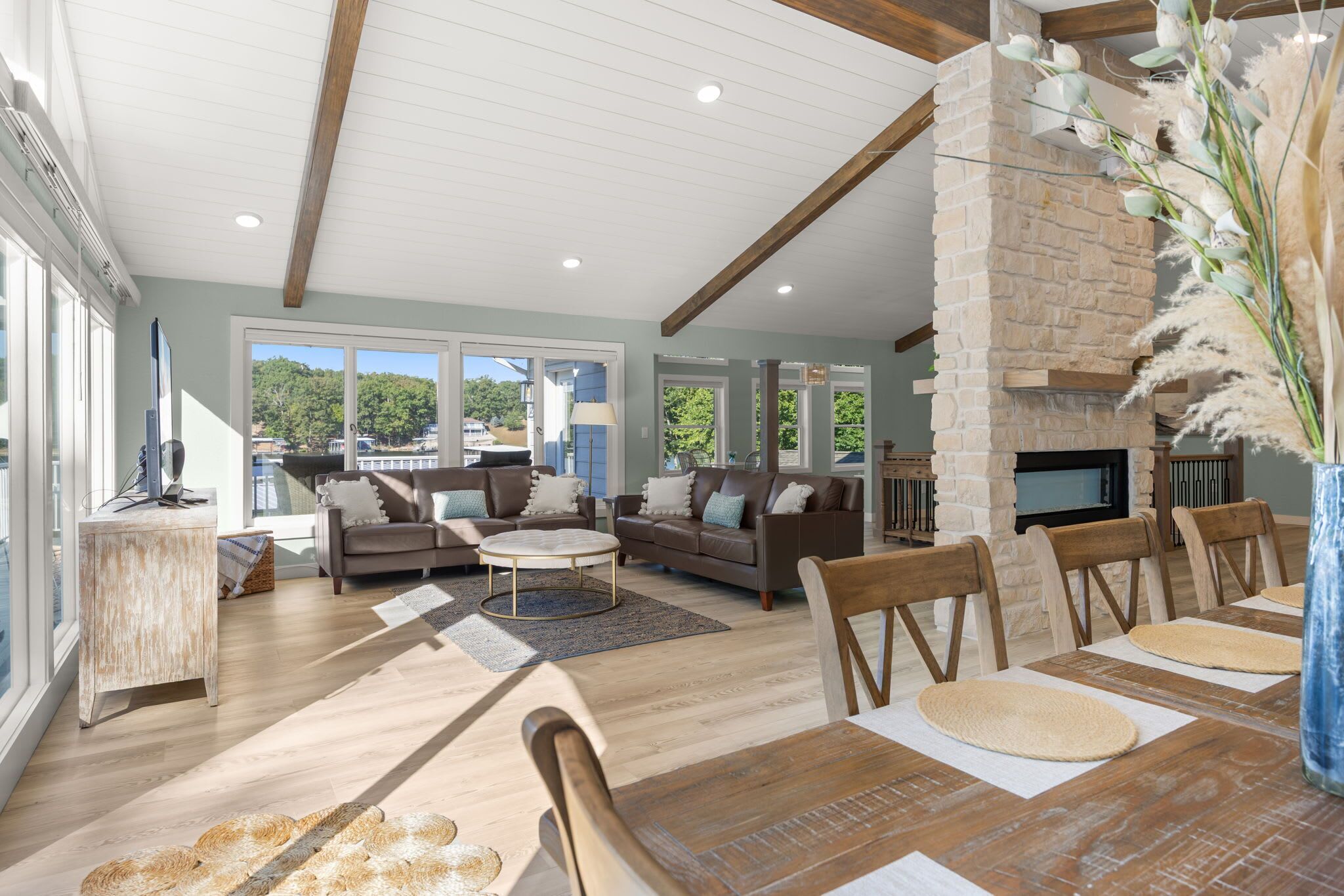 Amplia sala de estar con chimenea de piedra, ventanas grandes y comedor con muebles de madera.