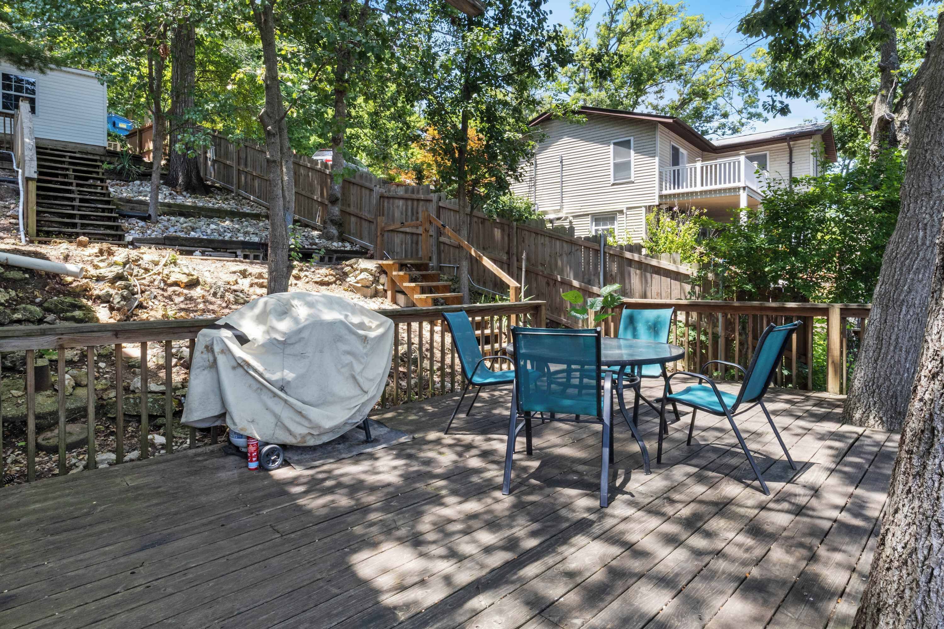 Une terrasse en bois avec des meubles d’extérieur, un barbecue couvert et un escalier en bois menant à une maison.