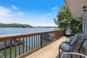 A wooden deck with a view of a lake, outdoor furniture, and a covered area with a lamp. - Lakefront Home With Huge Views and Great Fishing (Eldon)