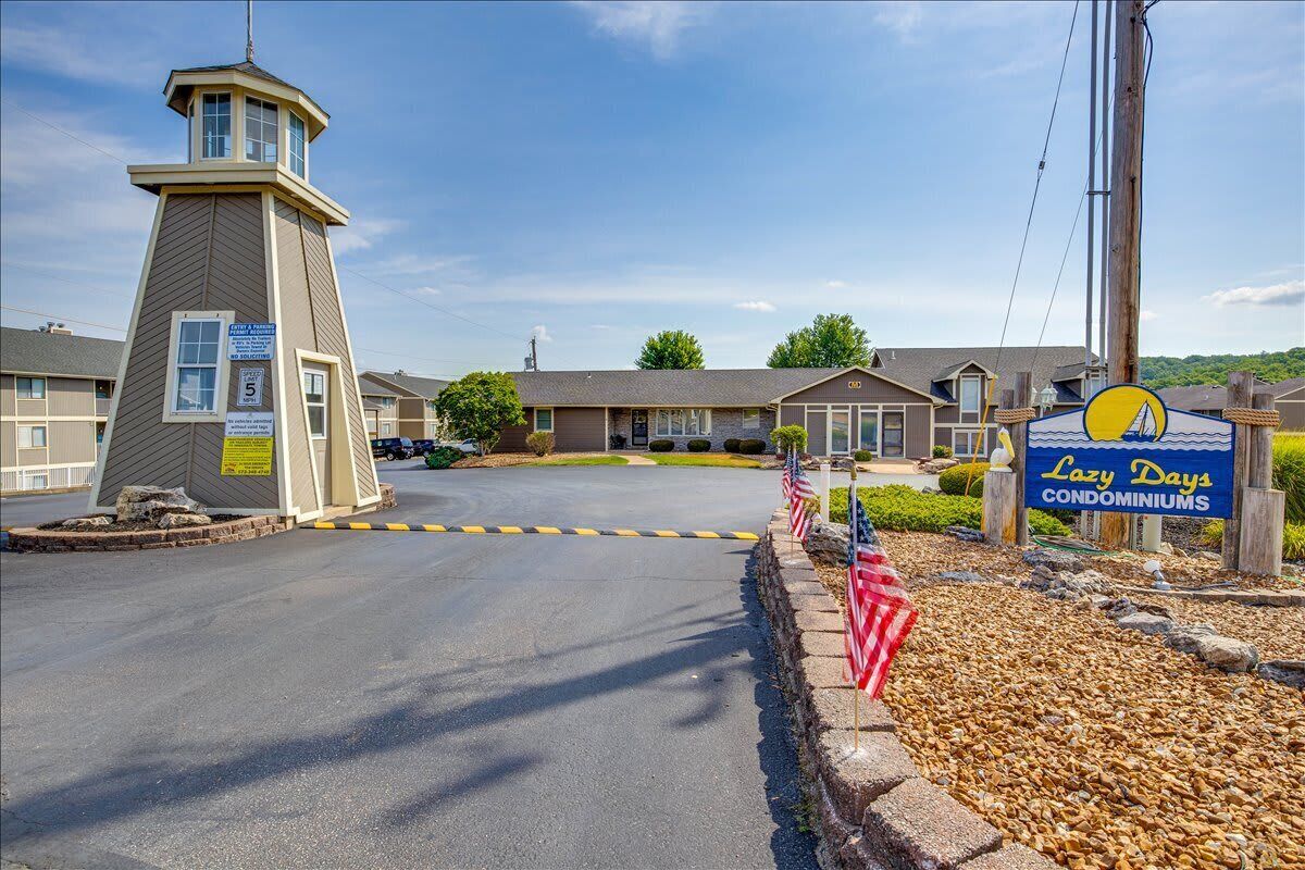 L’entrée d’un motel, avec une tour de guet, une enseigne indiquant « Lazy Days Condominiums » et des drapeaux américains le long de l’allée.