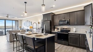 A modern kitchen with dark cabinets, a central island, and a dining area with chairs. - Waterview Retreat in Osage Beach With Public Dock and Community Pool (Osage Beach)