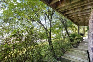 A covered wooden deck with a stone wall, surrounded by dense greenery and trees. - The Linn Creek Lodge Family Home With Private Dock (Linn Creek)