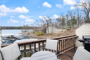 A deck with outdoor seating overlooking a lake, dock, and a small house. - Lakefront Condo Near Margaritaville (Osage Beach)