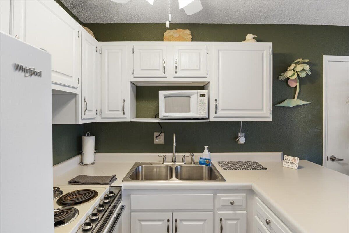 A kitchen with white cabinets, a microwave, a stove, and a sink.
