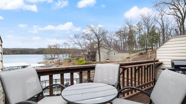 A deck with outdoor seating and a view of a lake and houses. - Lakefront Condo Near Margaritaville (Osage Beach)