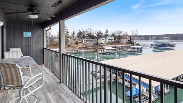 A balcony with a table and chairs, overlooking a marina with boats and houses. - Happy Harbor Lakefront Condo (Osage Beach)