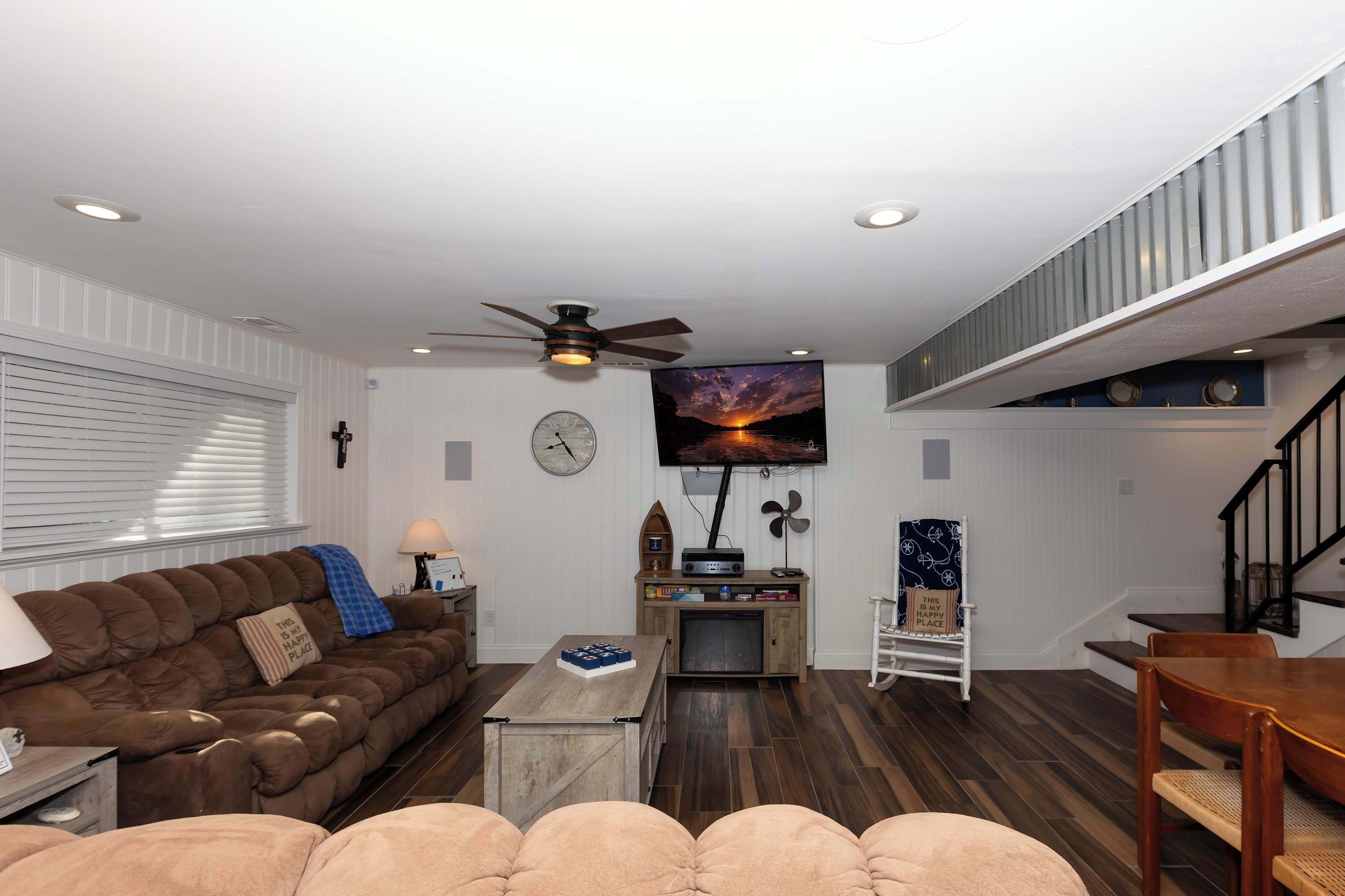A living room with a brown sofa, a coffee table, a TV, and a staircase.