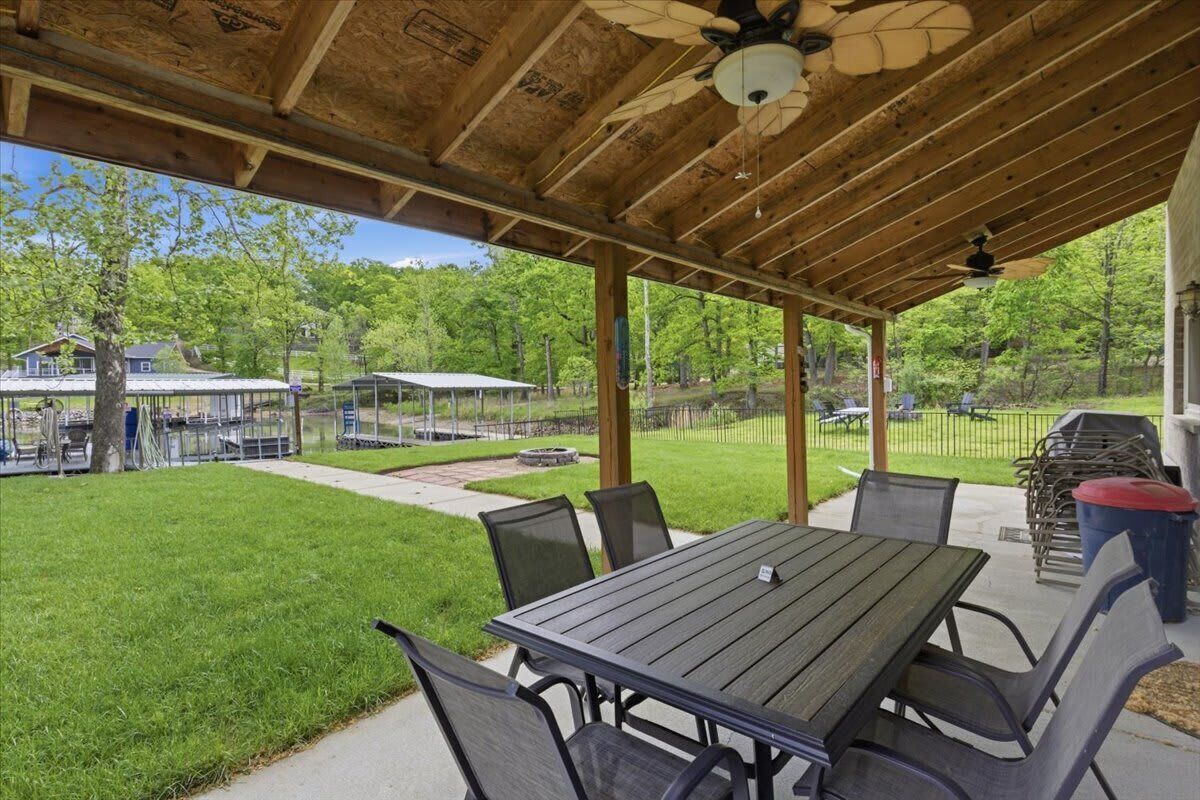 A covered patio with a table and chairs, a ceiling fan, and a view of a backyard with a grill and a fenced area.