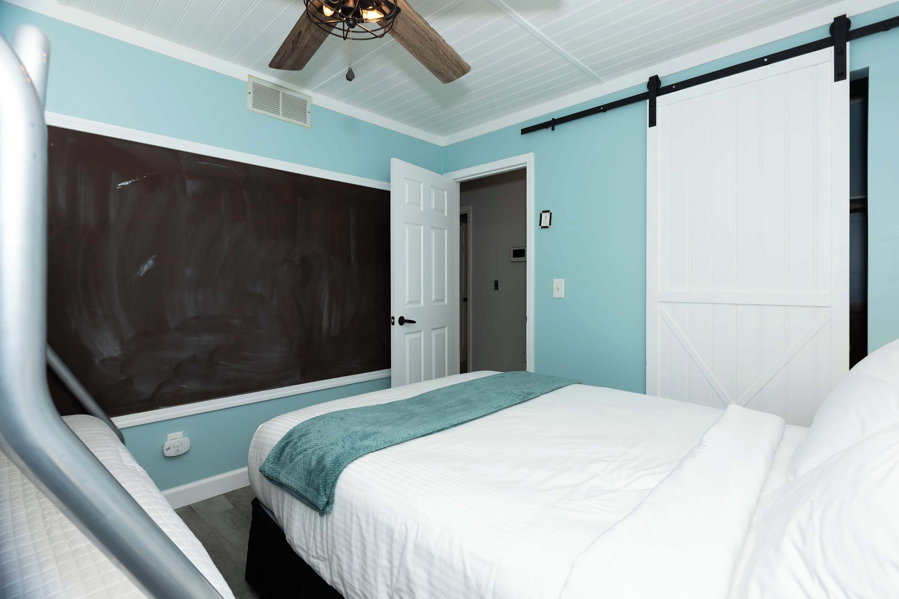 A bedroom with a bed, a ceiling fan, a door, and a wall with a dark panel.
