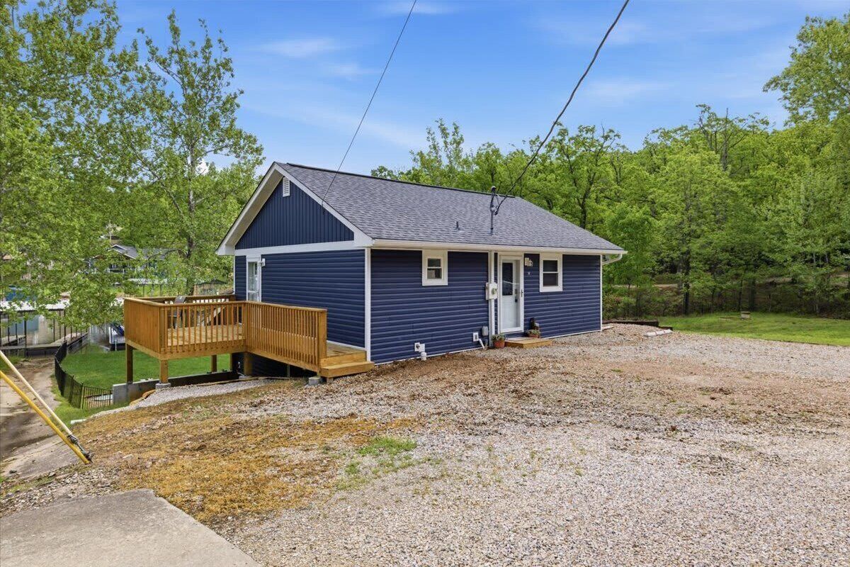 A single-story house with a front porch, a wooden deck, and a gravel driveway.