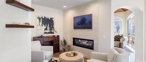 A modern living room with a fireplace, white sofas, and artwork on the walls.