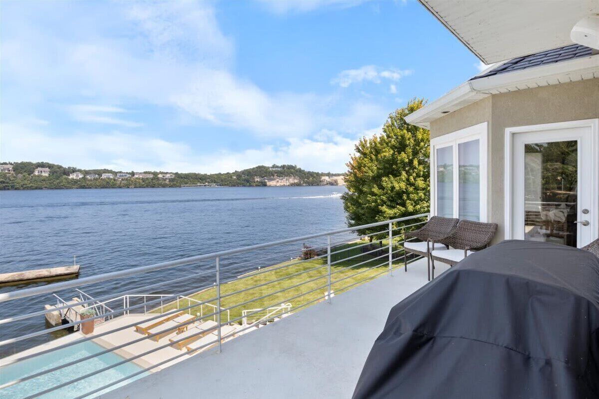 Ein Balkon mit Pool, Sitzgelegenheiten im Freien und Blick auf einen See sowie ferne Hügel.