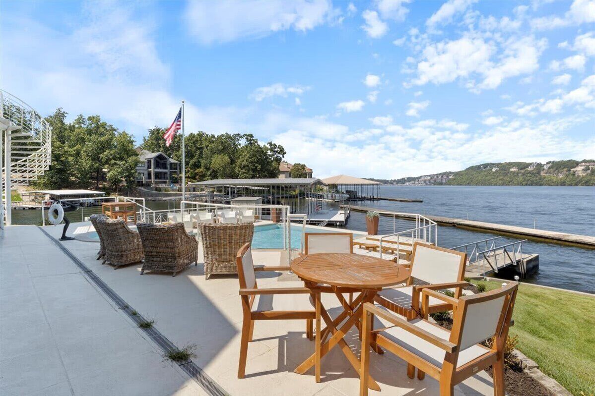 Un patio frente al agua con mobiliario exterior, piscina y vista al lago.