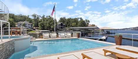 A rooftop pool area with lounge chairs, a flag, and a view of the water.