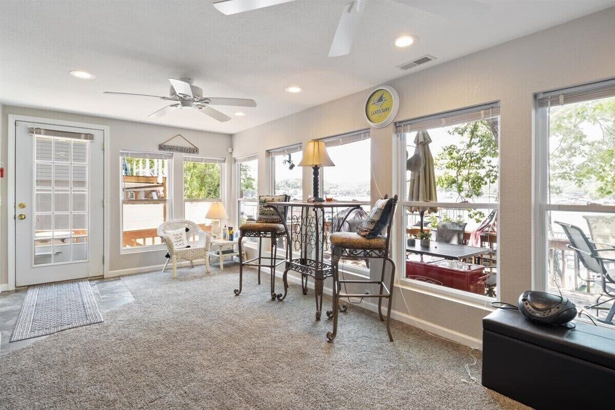 Une pièce spacieuse dotée d’un ventilateur de plafond, de grandes fenêtres, d’un coin repas avec des chaises et une table, et offrant une vue sur l’extérieur.