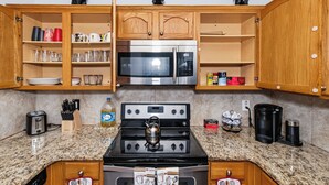A kitchen with wooden cabinets, a stainless steel microwave, a gas stove, and various kitchen utensils.