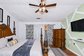 A bedroom with a bed, a wooden dresser, a television, and a ceiling fan.
