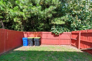 A fenced backyard with a red wooden fence, a grassy area, and two trash bins.