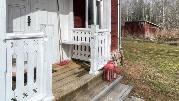 A wooden porch with white railings, a red door, and a red lantern. - 2 Person Holiday Home in Morlunda (Mörlunda)
