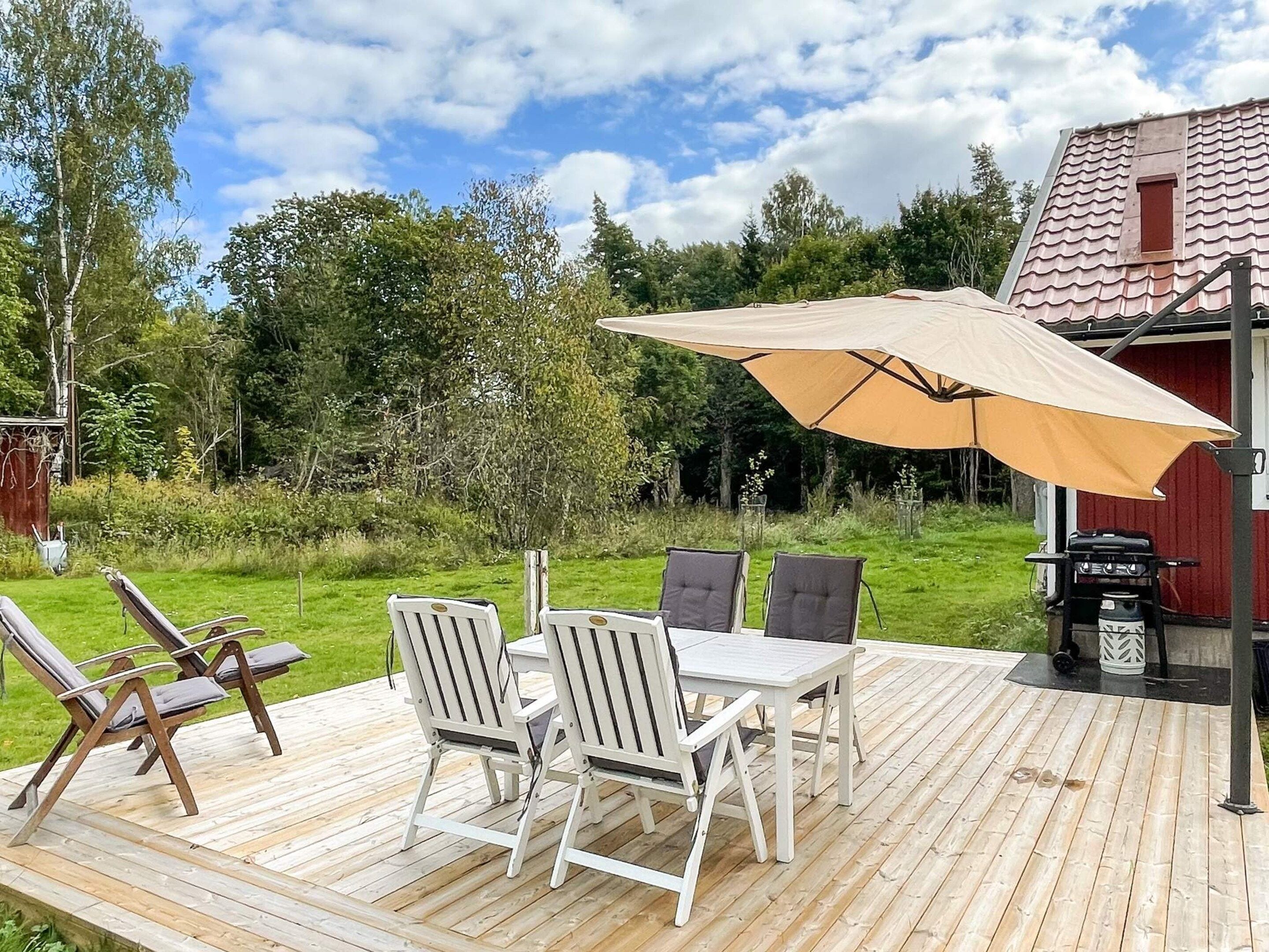 A wooden deck with a table and chairs, an umbrella, and a grill.