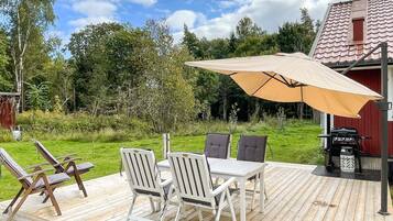 Una terraza de madera con una mesa, sillas, una sombrilla y una parrilla.