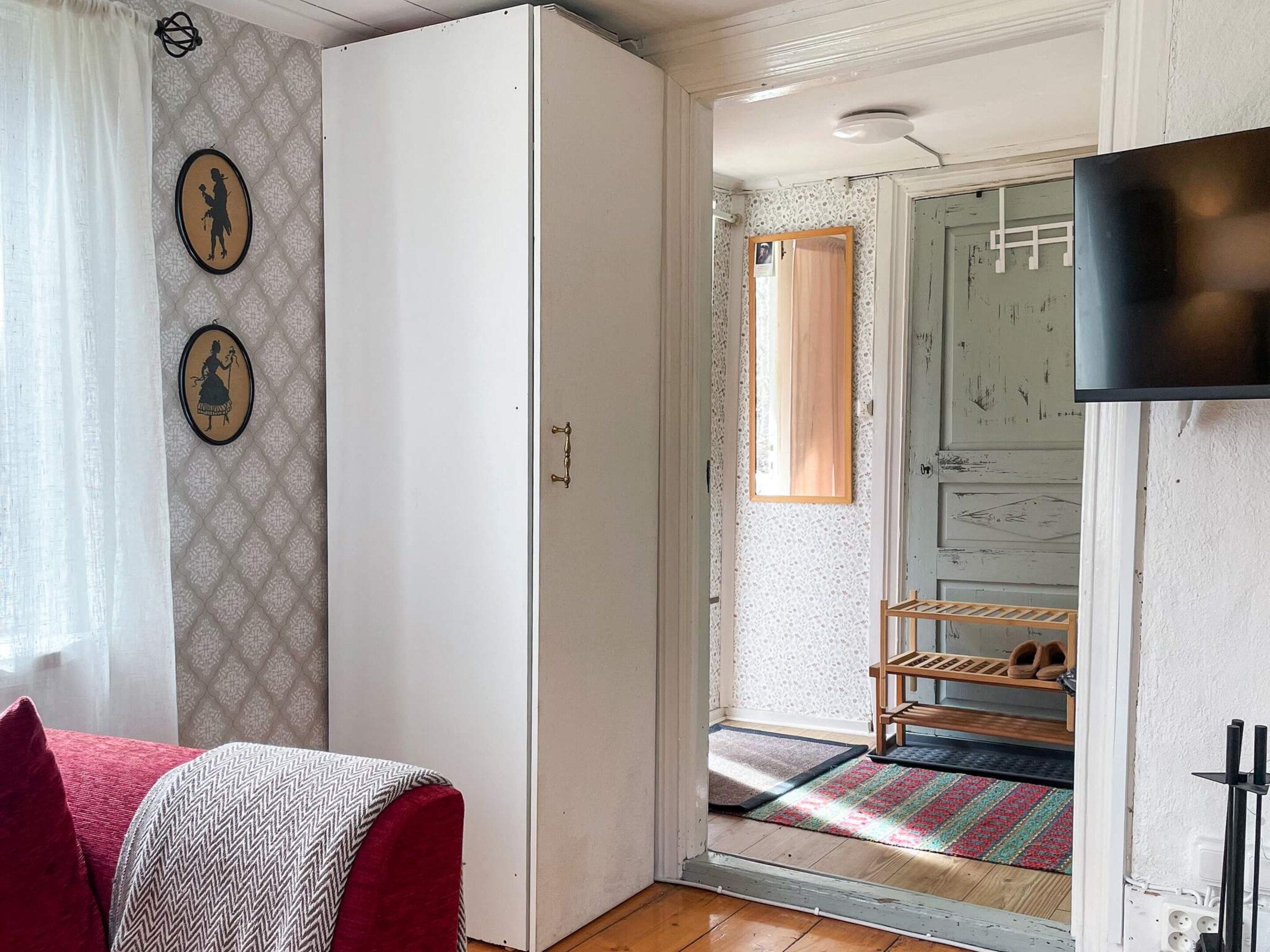 Una habitación con armario, cama con colcha estampada, pared con marcos decorativos, puerta con espejo y zapatero.