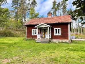 Ein kleines, einstöckiges Holzhaus mit einem roten Ziegeldach, einer Veranda und einem Rasen.
