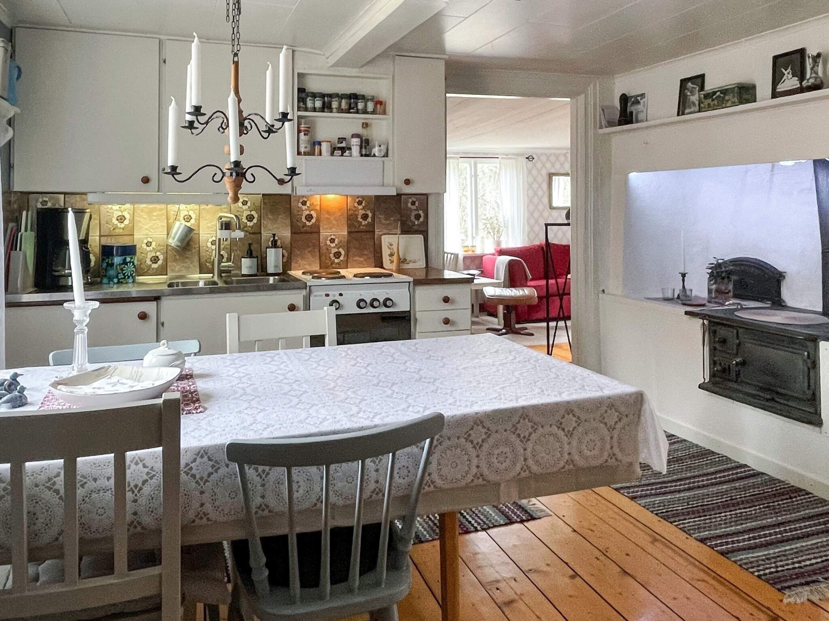 A compact kitchen with a dining area, wooden flooring, and a red sofa in the background.