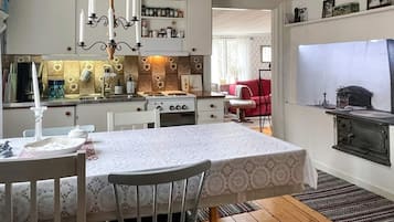 A compact kitchen with a dining area, wooden flooring, and a red sofa in the background.